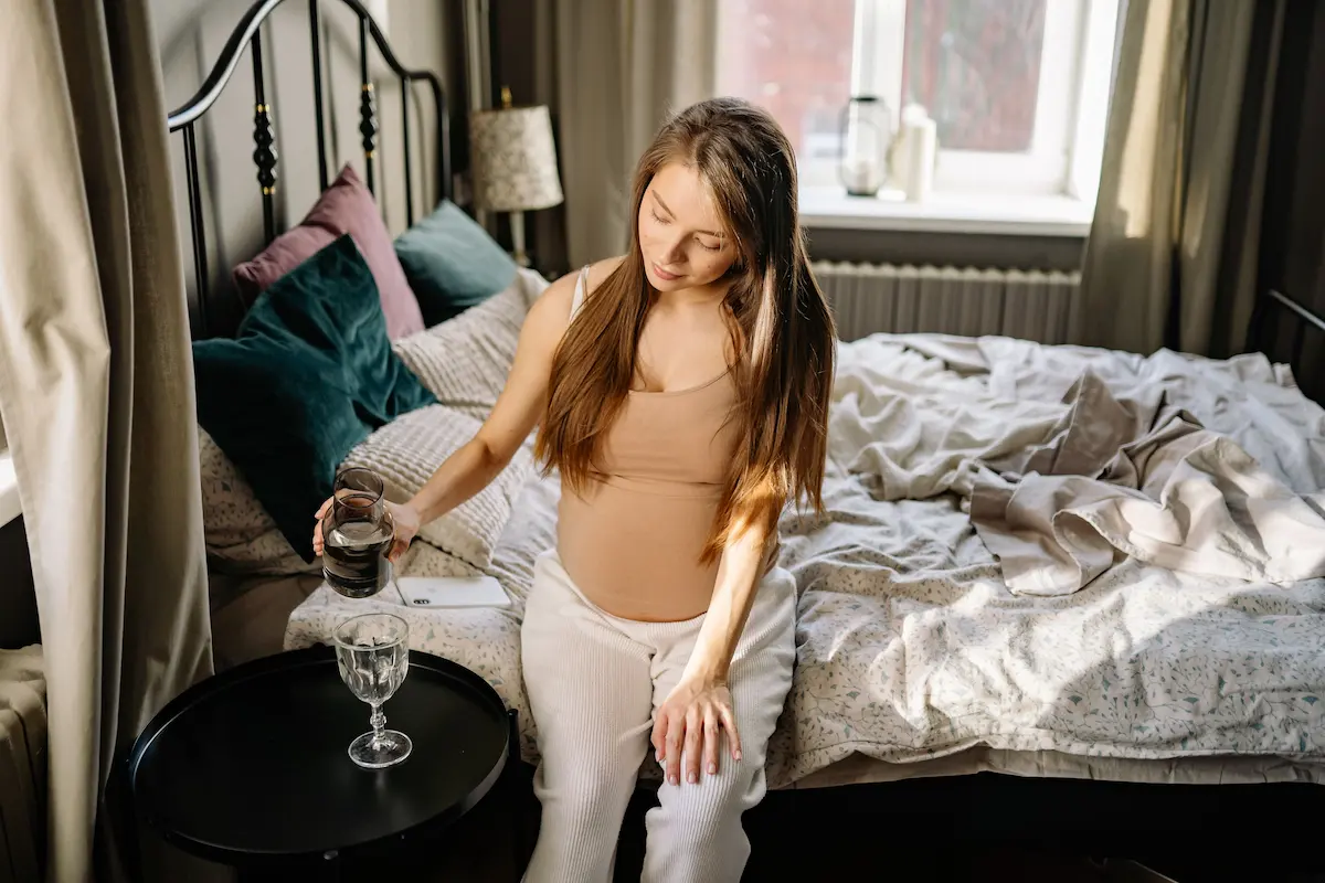 Multivitamin gravid: Gravid kaukasisk kvinne som sitter på sengen og nyter et rolig øyeblikk under svangerskapet, relevant for svangerskapsvelvære og kosttilskudd.