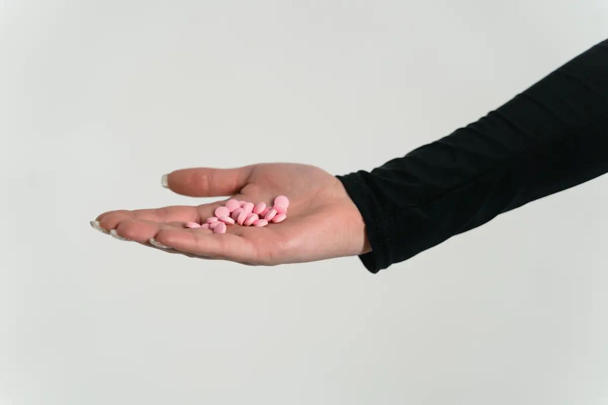 Multivitamin former: Nærbilde av en utstrakt hånd som holder rosa piller mot en hvit bakgrunn, ideelt for temaer som kosttilskudd, vitaminer og helseprodukter.