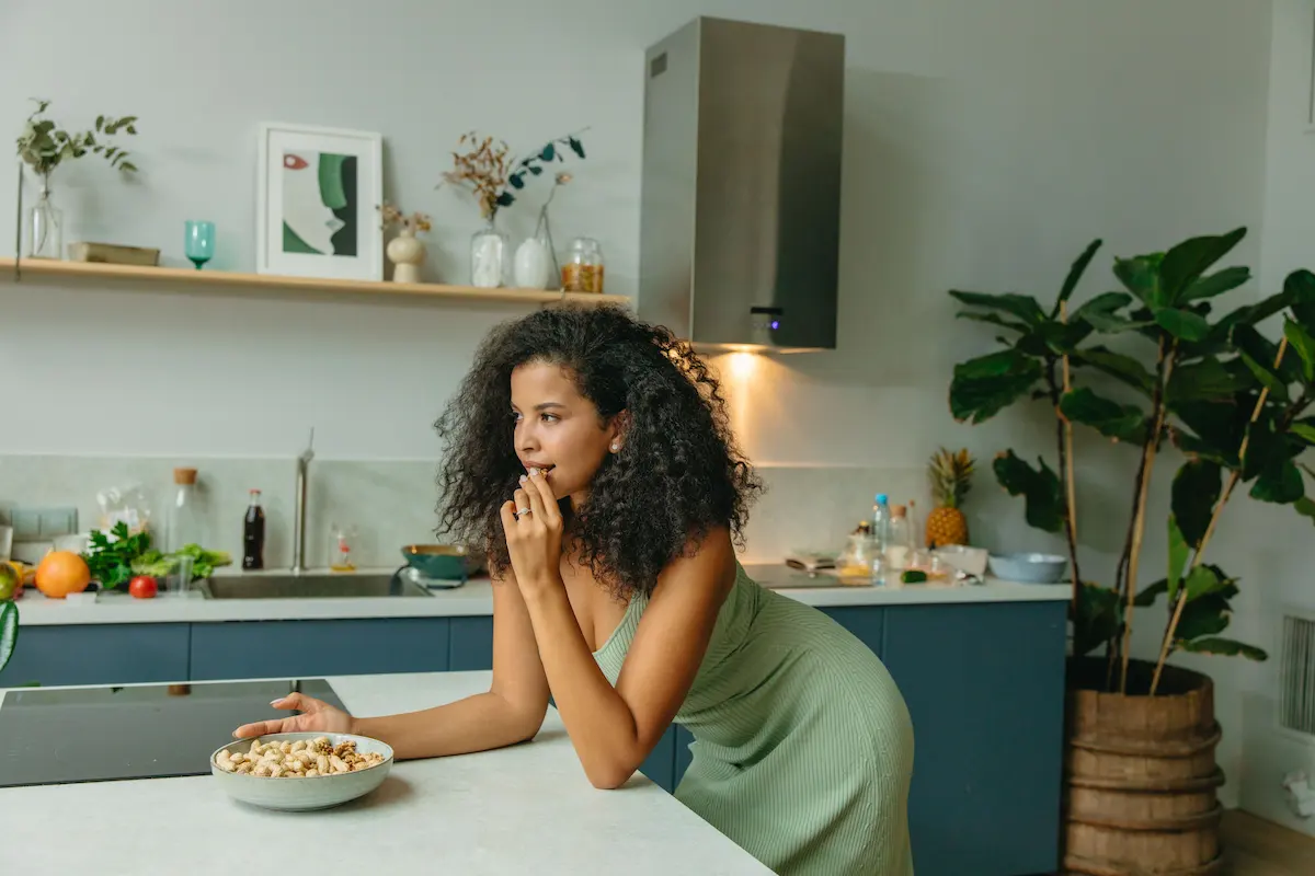 Hva er multivitamin: Kvinne i grønn kjole som spiser et sunt mellommåltid i et moderne kjøkken, perfekt for temaer som sunn livsstil, kosthold og kosttilskudd.