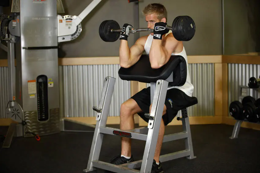 Preacher curl sluttposisjon med stanga curlet opp mot skuldrene og biceps sammentrukket