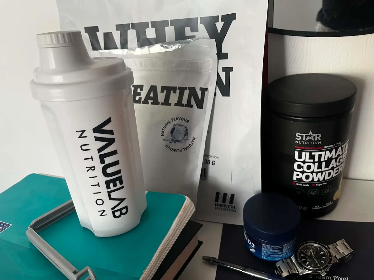 Bilde av proteinshaker sammen med andre kosttilskudd på et bord.
